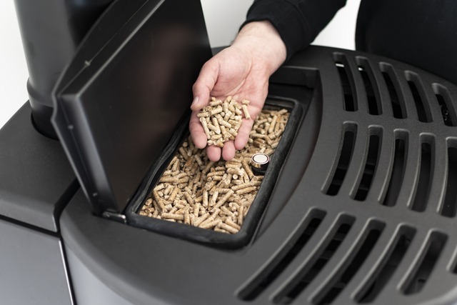 Pellet Stove, Man Holding Granules In His Hand Above A Modern Black Stove